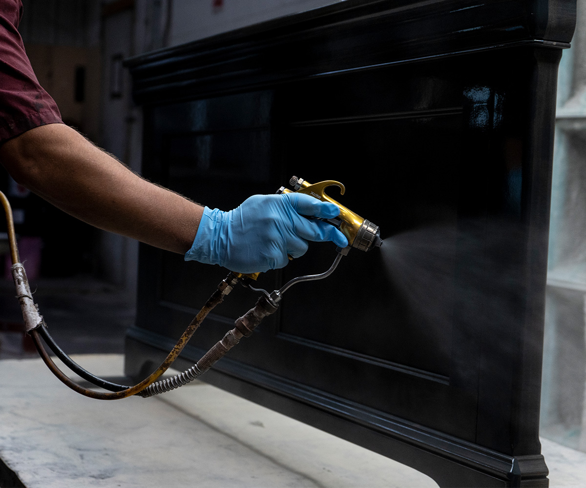 Craftsperson spray-finishing a dark wood furniture piece by hand.