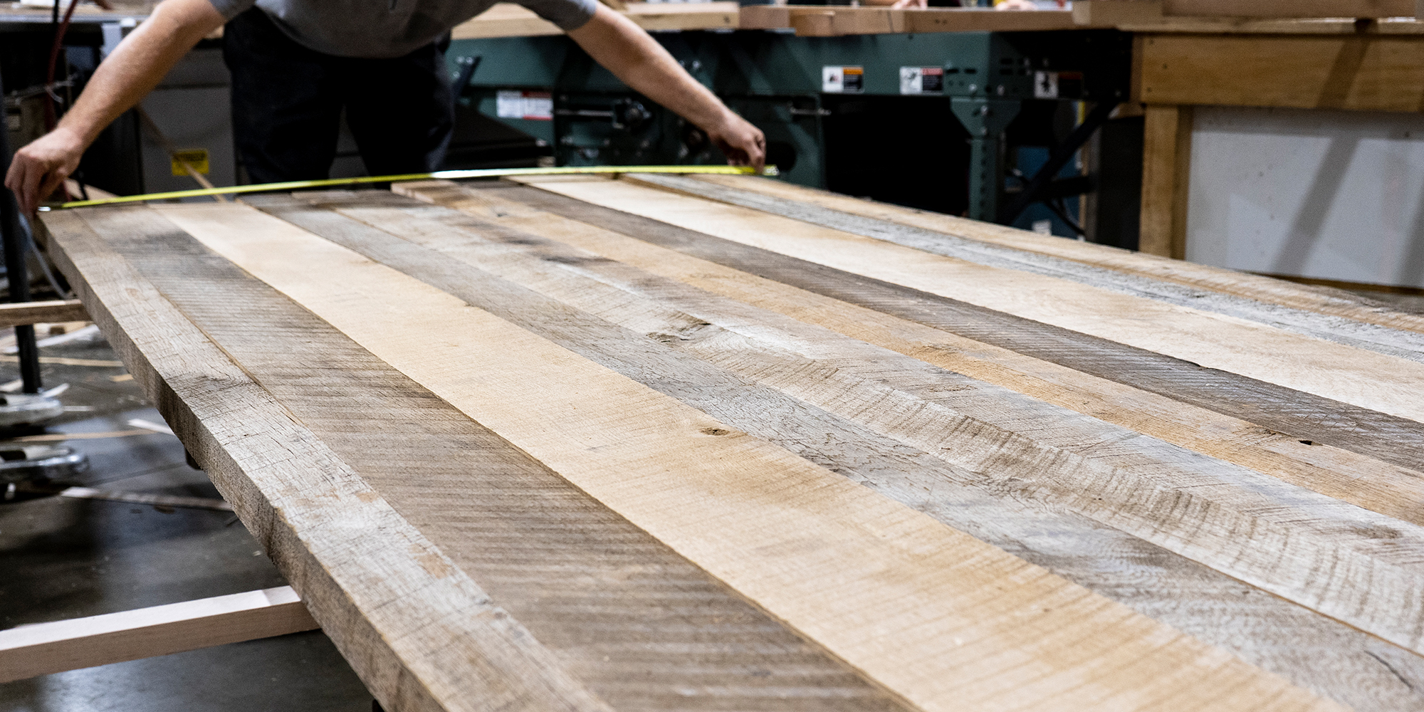 Craftsperson measuring reclaimed hardwood boards in a furniture workshop.
